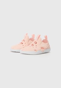Világos rózsaszín Nike sportcipők, sima, rugalmas felsőrésszel, több szellőzőlyukkal, fehér talppal és hátsó húzófülekkel a könnyű felhúzáshoz.