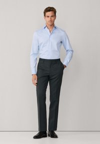 Lichtblauw overhemd met lange mouwen en een gestructureerde kraag, gecombineerd met donkere, op maat gemaakte broek en zwarte leren schoenen, staand tegen een neutrale achtergrond.