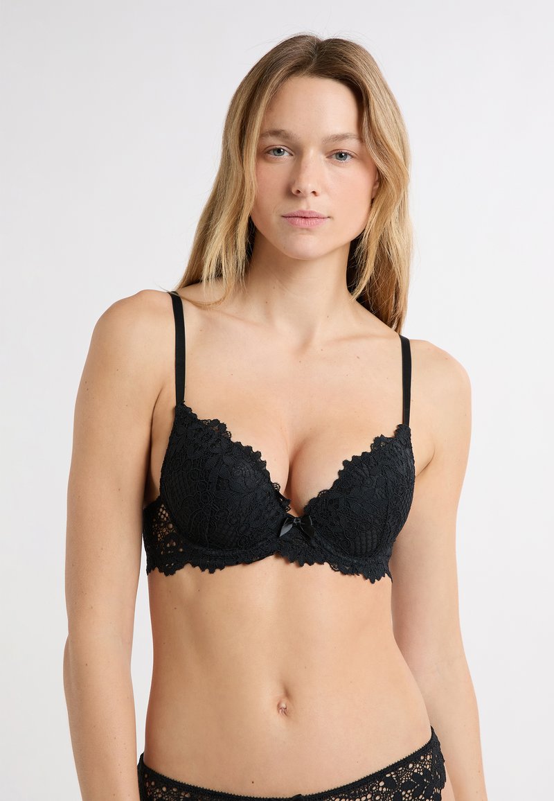 Schwarzer Push-up-BH aus Spitze mit gewellten Rändern, dünnen verstellbaren Trägern und einer Schleife in der Mitte. Durchgehend mit strukturiertem Blumenmuster.