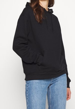 Black hoodie made of cotton fabric, featuring a front pouch pocket, drawstring hood, and ribbed cuffs and hem. Paired with blue jeans.
