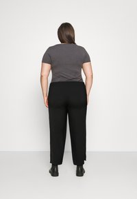 Chemise grise à manches courtes et pantalon large noir, visibles de dos, associés à des bottines, sur un fond blanc uni.