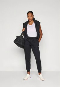 Melnas sporta drēbes ar bezroku topu un svītrainām biksēm ar pieguļošu siluetu. Kopā ar baltām sporta kurpēm un melnu duffle somu.