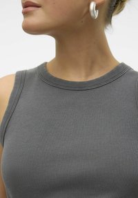 Grijze geribbelde tanktop met een ronde halslijn en brede banden, gecombineerd met een metalen ringoorbel, die textuur en een aansluitend ontwerp laat zien.