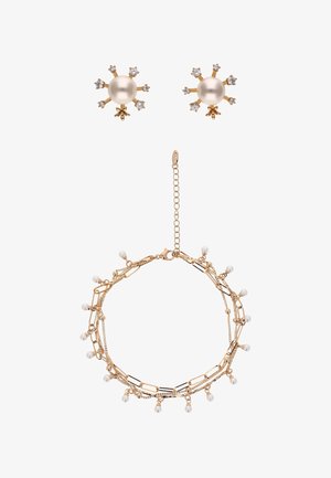 Naszyjnik w złotym odcieniu z małymi białymi perłami i ogniwami łańcuszka, zestawiony ze złotymi kolczykami wkrętami z centralną perłą otoczoną małymi kryształkami.