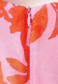 Gros plan d'un tissu rose avec de grands motifs floraux orange et une fermeture éclair rose fermée au centre.