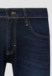 Dunkelblaue Jeans aus Denim mit gelben Kontrastnähten, schwarzer Knopfverschlüsse, Gürtelschlaufen und sichtbaren vorderen Taschen.