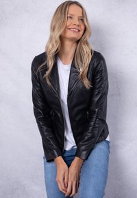 Fitted black leather jacket with a smooth texture, diagonal zipper, and two side pockets. Worn over a white t-shirt and blue jeans.