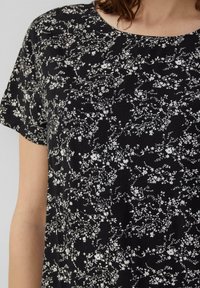 Zwarte stoffen t-shirt met een witte bloemenpatroon, korte mouwen en een ronde halslijn. Zachte textuur met een ontspannen pasvorm.