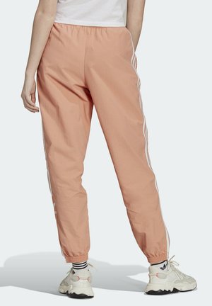 Peach-colored athletic pants with an elastic waistband, tapered cuffs, white side stripes, and subtle branding on the lower leg.