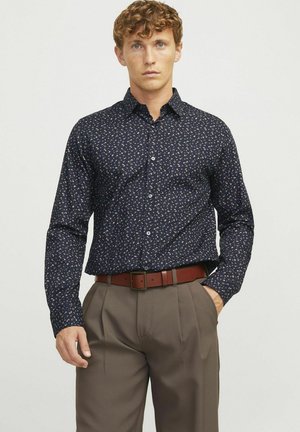 Navy button-up shirt with a floral pattern in beige, long sleeves, and a collar. Paired with light brown trousers and a brown belt.