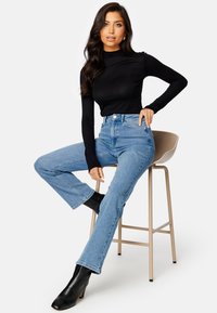 Czarny top z długim rękawem, jasnoniebieskie dżinsy z wysokim stanem oraz czarne botki na obcasie. Gładki materiał i zwężające się nogawki z delikatnymi przetarciami.