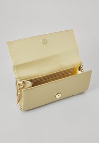 Gold metallic clutch bag with a snap closure, chain strap, and interior pockets, featuring a smooth texture and minimalist design.