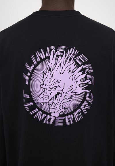 Schwarzes T-Shirt mit einem großen, lila Drachenmotiv auf der Rückseite, mit kreisförmigen Linien und dem Text "JLindberg", der in das Design integriert ist.