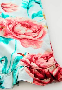Bloemenpatroon stof met grote roze rozen op een lichtblauwe achtergrond. Gerimpelde zoom met rode accentstiksel voegt detail toe.
