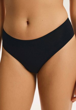 Close-up of person wearing plain black bikini-style underwear, showing abdomen and upper thighs against a neutral background.