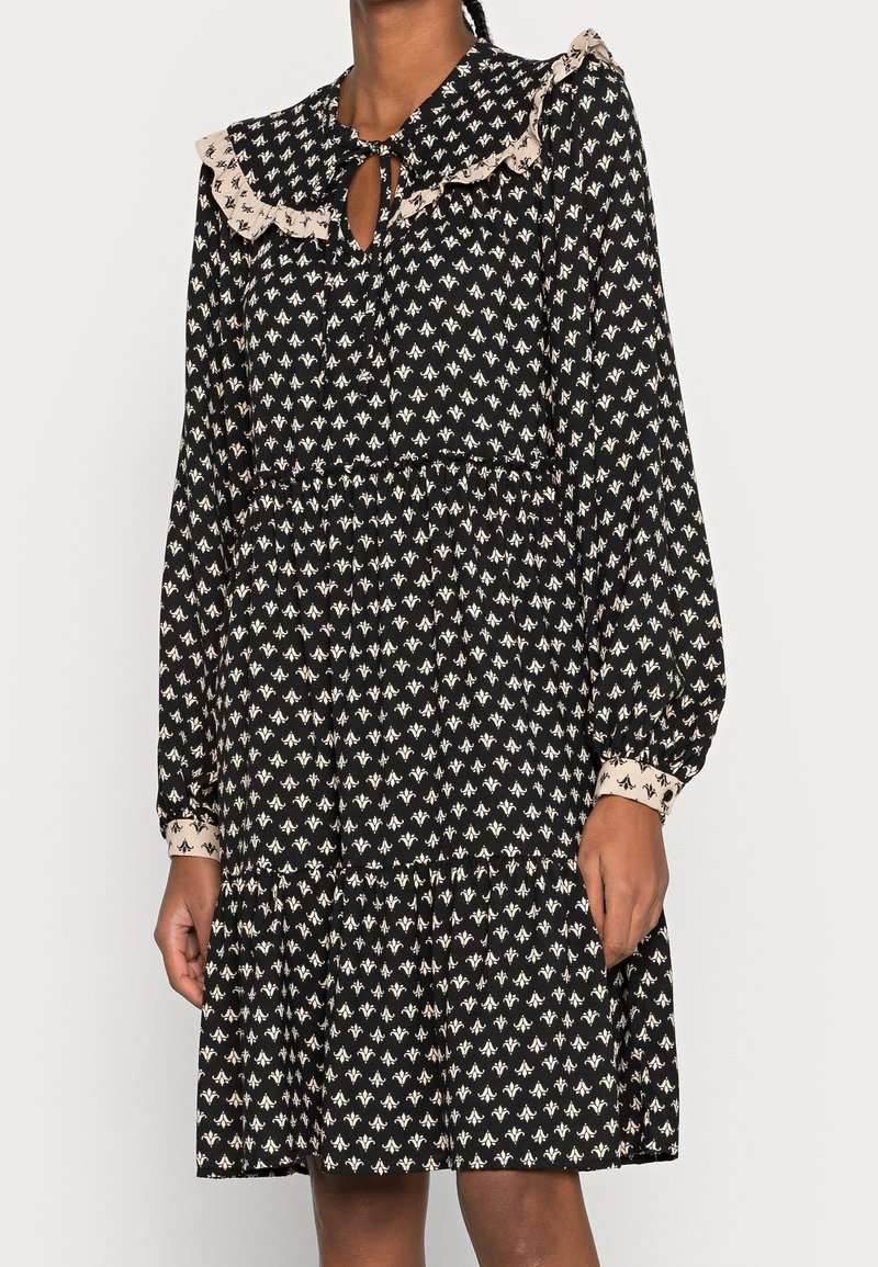 Robe noire avec motif floral ivoire, col à volants, ouverture en forme de goutte, manches longues et jupe à volants, confectionnée dans un tissu léger.