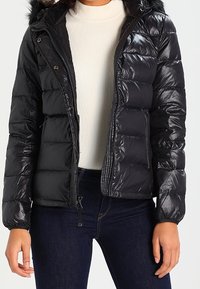Sort pufferjakke med en glat overflade, udstyret med lynlås foran, aftagelig hætte med falsk pelskant og vandret quiltet design.