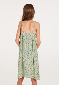 Groene bloemenjurk met dunne bandjes, lichte stof en een ontspannen pasvorm, met een geplooide achterkant en bloemen schetsen in zwart-wit.