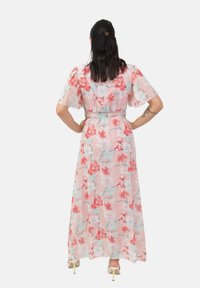 Robe maxi florale en tissu rose doux, avec des manches courtes, une taille élastique et une silhouette fluide ornée de fleurs rouges et vert menthe.