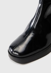 Black leather ankle boot with a rounded toe, glossy finish, and a textured black sole. Features a smooth side seam detail.