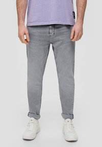 Pantalones vaqueros de mezclilla gris con corte tapered, lavado claro, diseño de cinco bolsillos y dobladillos enrollados, combinados con zapatillas blancas y una camiseta de color lavanda.