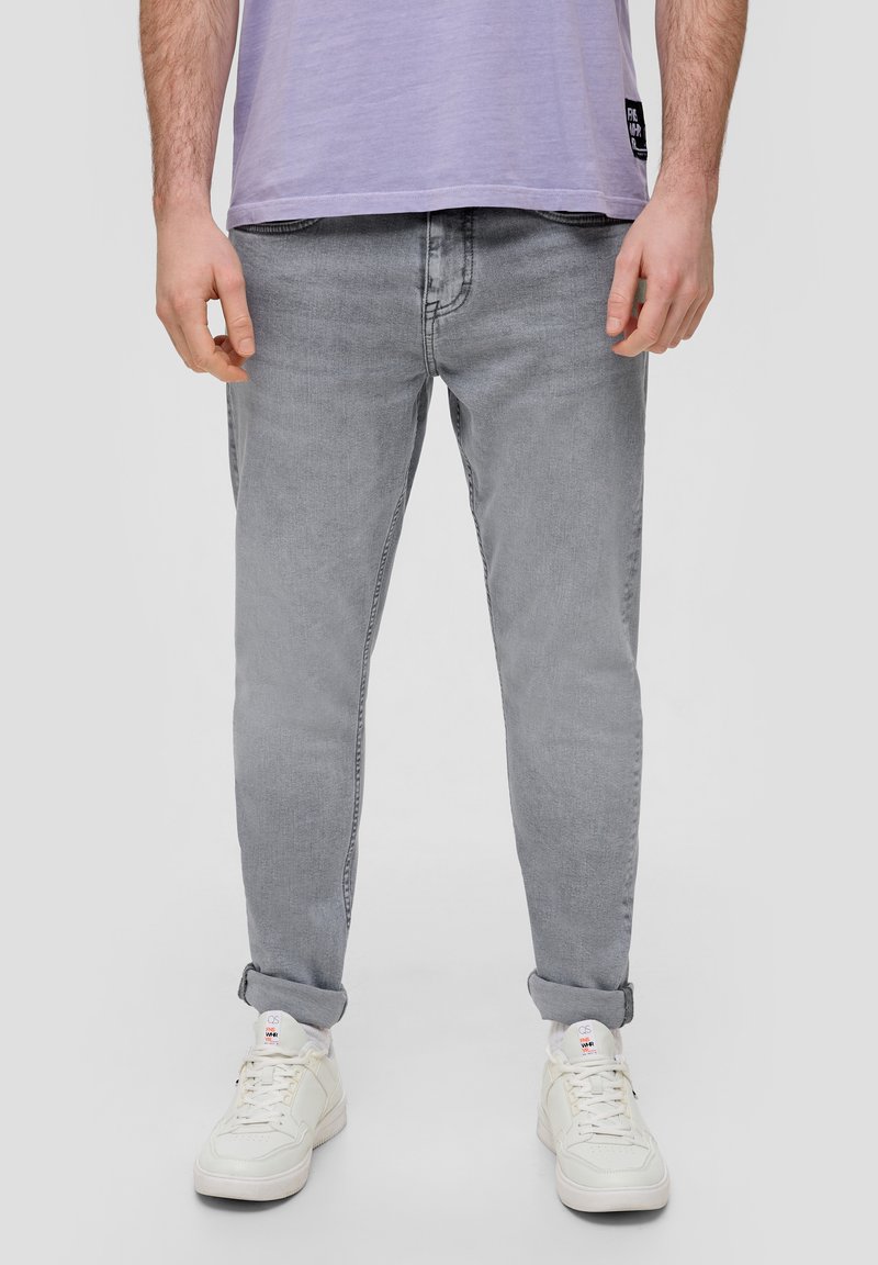 Pantalones vaqueros de mezclilla gris con corte tapered, lavado claro, diseño de cinco bolsillos y dobladillos enrollados, combinados con zapatillas blancas y una camiseta de color lavanda.