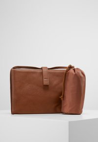 Borsa in pelle marrone con finitura testurizzata, dotata di una cintura frontale e di un sacchetto compatto con coulisse di un tono di marrone più chiaro.