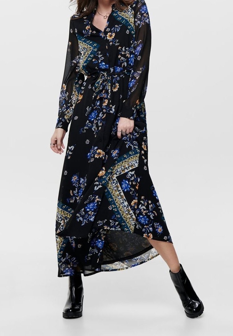Robe fluide noire à manches longues, motifs floraux en bleu et jaune, design portefeuille, et longueur cheville. Stylisée avec des bottines noires.