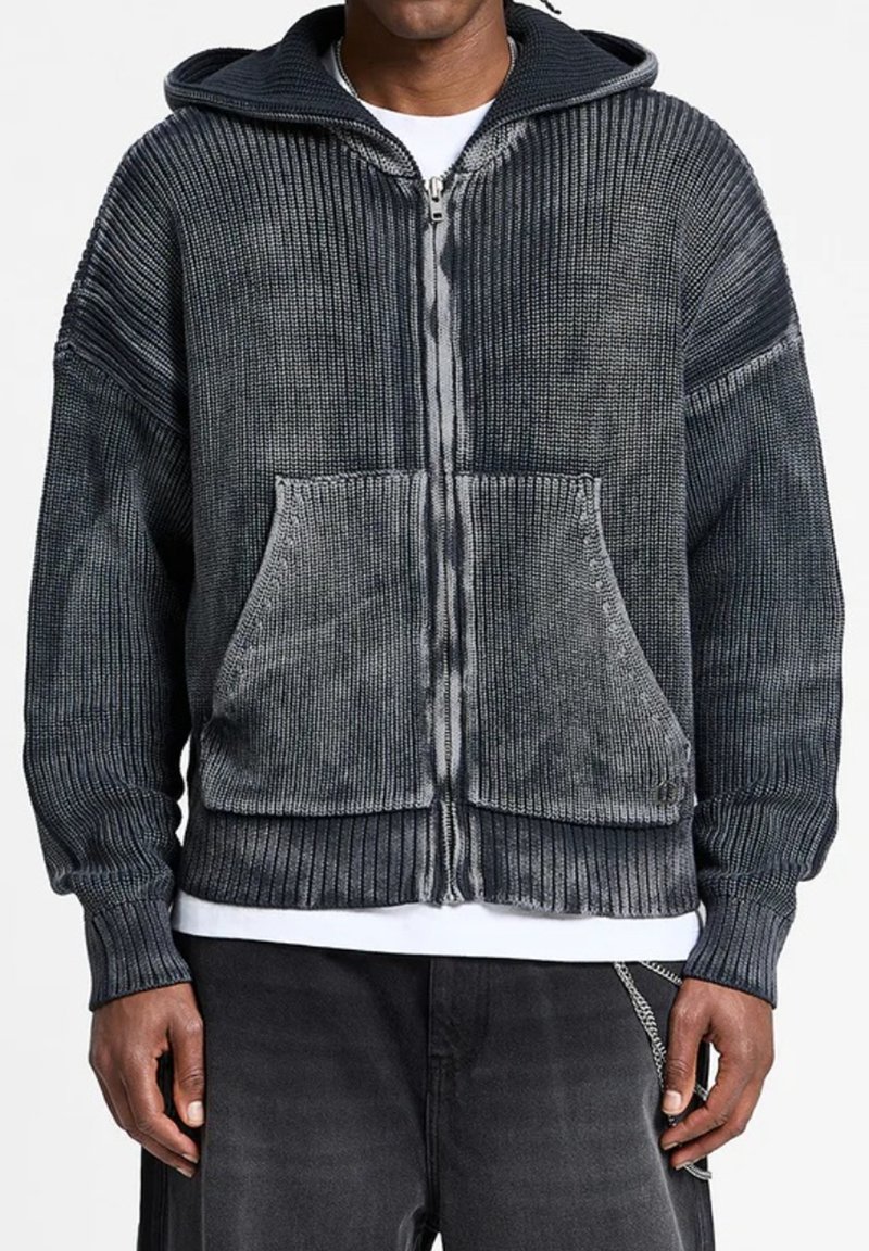 Felpa grigia con cappuccio, zip e texture a costine, tasca frontale e un leggero sbiadimento. Presenta una cerniera a contrasto lungo il centro.