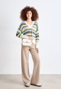 Maglione soffice multicolore con strisce blu, verdi e bianche; pantaloni beige a gamba larga; borsa a tracolla crema; sneakers argentate.