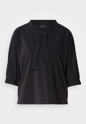 Blouse noire avec un col rond, détail de nœud au niveau du cou et manches courtes bouffantes. Le tissu présente une texture côtelée subtile.