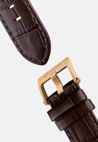 Bracelet de montre en cuir marron avec des coutures visibles, doté d'une boucle en métal doré et d'un détail de logo embossé.