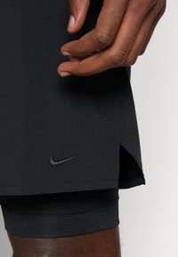 Black athletic shorts with a side slit and textured inner lining. Features a small black Nike logo. Lightweight, stretchable fabric.