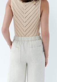 Top in maglia beige con motivo a zigzag, abbinato a pantaloni in lino grigi chiari con vestibilità rilassata e due tasche posteriori.