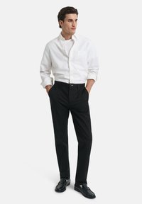 Camicia bianca con bottoni, pantaloni neri e mocassini neri. La camicia ha una tasca e i pantaloni presentano un design a gamba dritta. Linee semplici e pulite.