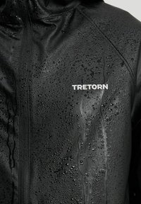 Vattentålig svart jacka i glänsande material, med synliga vattendroppar, och "TRETORN" logotyp i vitt på framsidan.