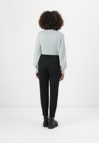 Lichtblauwe gebreide trui met ballonsleeves, gecombineerd met zwarte tapered broek en chunky zwarte enkellaarzen, gezien vanaf de achterkant.