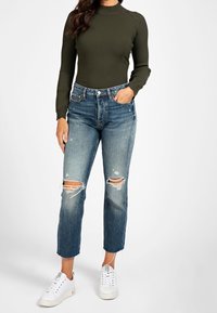 Olijfgroene geribde lange mouw top gecombineerd met distressed lichtblauwe jeans met scheuren op de knieën en witte lage sneakers.