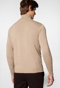 Beżowy sweter dzianinowy z wysokim kołnierzem, dopasowanymi rękawami i ściągaczem na dole, prezentujący gładką fakturę i subtelne detale w przeszyciach.