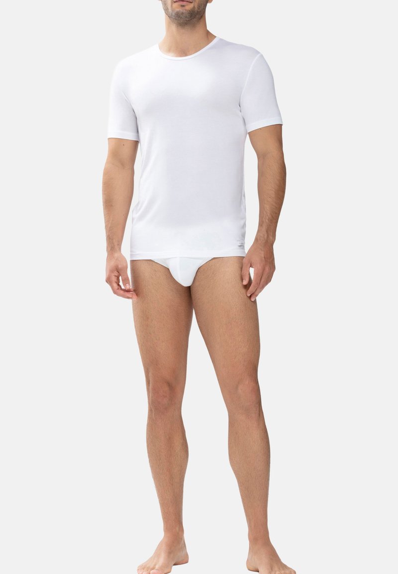 T-shirt blanc à manches courtes avec un col rond, fabriqué en tissu léger, accompagné de culottes blanches assorties, sur un fond neutre.