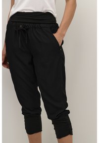 Pantalons noirs 3/4 avec une taille élastique, cordon de serrage et poignets froncés. Fabriqués en tissu léger, ils disposent de poches latérales.