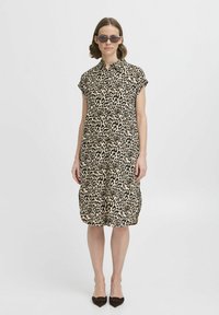Abito camicia con stampa leopardata in beige e nero; maniche corte, chiusura con bottoni davanti; lunghezza al ginocchio con vestibilità rilassata; abbinato a ballerine e occhiali da sole.