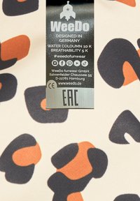 Mönstrad tyg med överdimensionerade svarta och orangea fläckar på en gräddvit bakgrund. Etikett med skötselråd och varumärkesdetaljer synlig.
