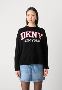 Černý pletený svetr s červeným a bílým textem "DKNY NEW YORK", žebrovanými manžetami a spodním lemem. Kombinován s světle modrou džínovou sukní.