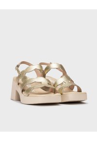 Sandalias de tacón metálicas doradas con un diseño de tira trenzada texturizada y suela de plataforma gruesa beige. Incluye correa ajustable en el tobillo.
