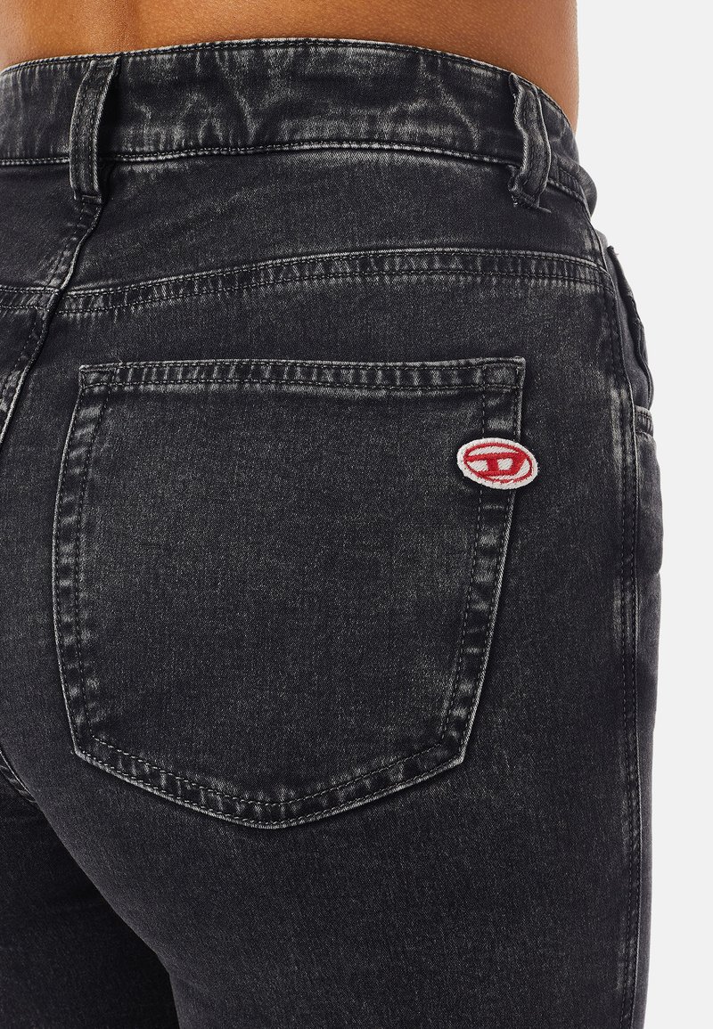 Primo piano di una persona che indossa jeans in denim grigio scuro con una tasca posteriore visibile e un piccolo dettaglio di toppa rossa e bianca.