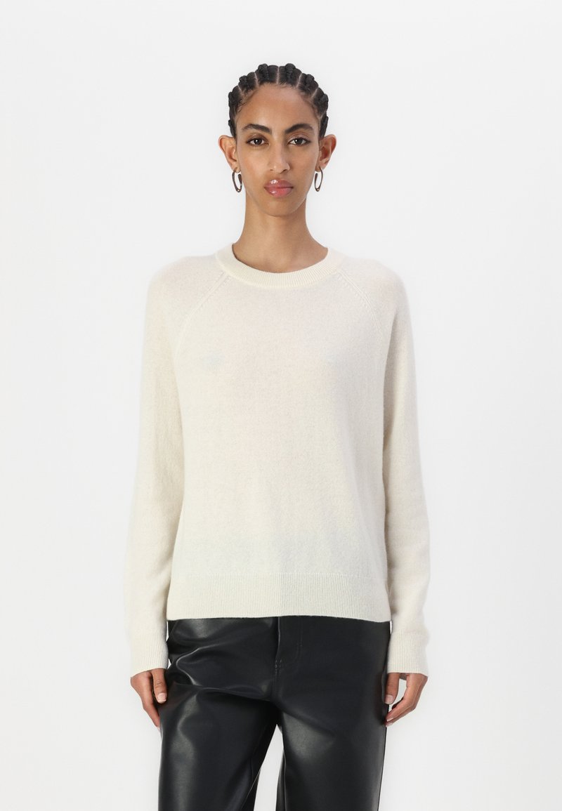 Ljusbeige ulltröja med raglanärmar och ribbat halsband. Mjuk textur med en enkel design, kombinerad med svarta läderbyxor.