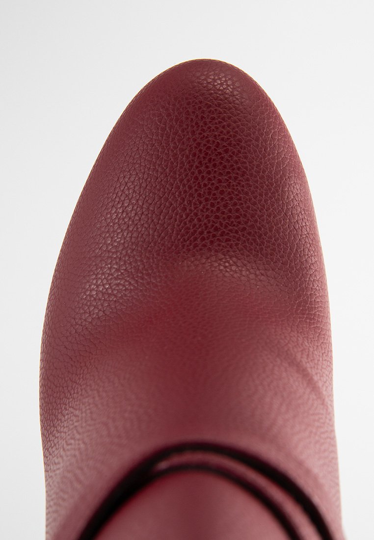 Scarpe in pelle bordeaux con una superficie testurizzata, punta arrotondata e un design dell'arco liscio. Accenti minimi e nessun dettaglio hardware visibile.