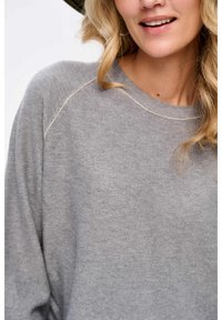 Szary dzianinowy sweatshirt o luźnym kroju, z okrągłym dekoltem i lekko widocznymi detalami przeszycia wzdłuż szwów ramion.