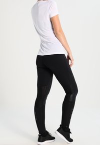 Black athletic leggings with mesh panels, paired with a fitted white striped t-shirt. The outfit is complemented by black sneakers.